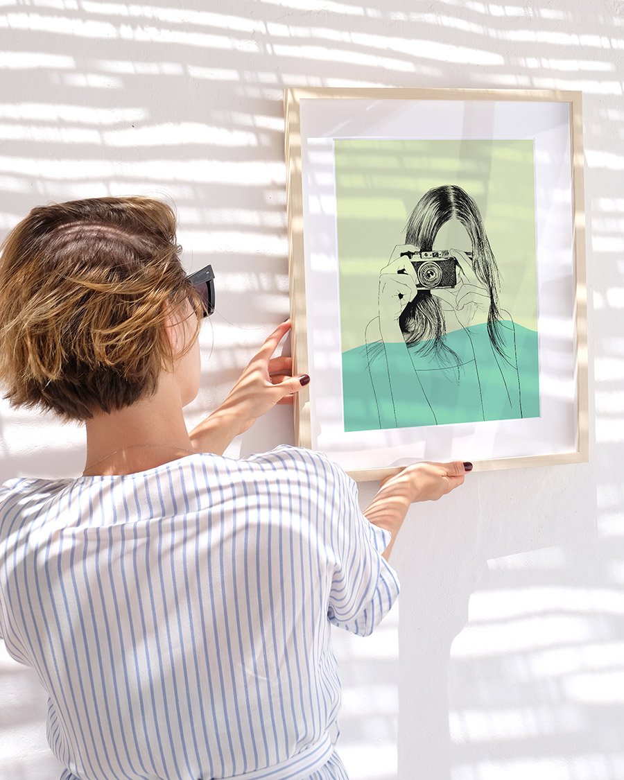 mulher a segurar em quadro com ilustração de outra mulher a tirar uma fotografia